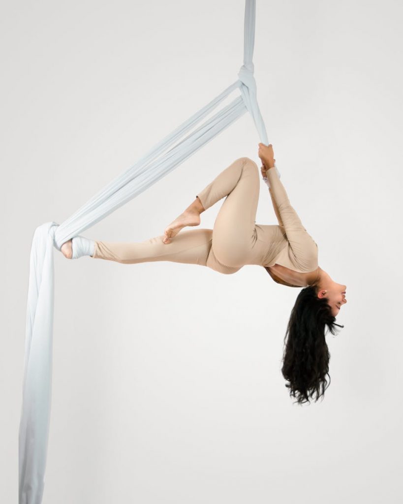Woman in Beige Clothing Performing Tricks on Aerial Silks